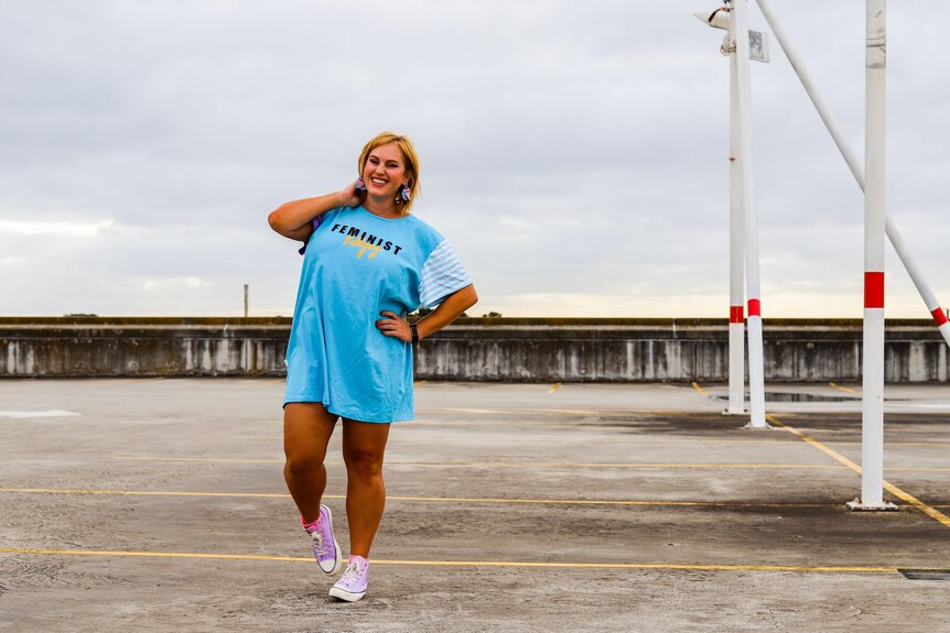 Jen stands in a rooftop carpark modeling a baby blue shirt that reads 'feminist killjoy'