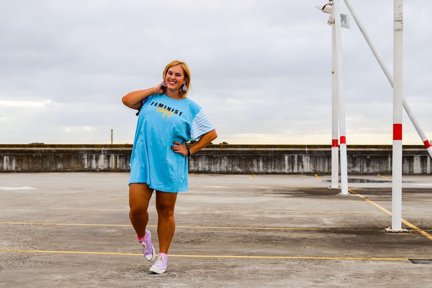 Jen stands in a rooftop carpark modeling a baby blue shirt that reads 'feminist killjoy'