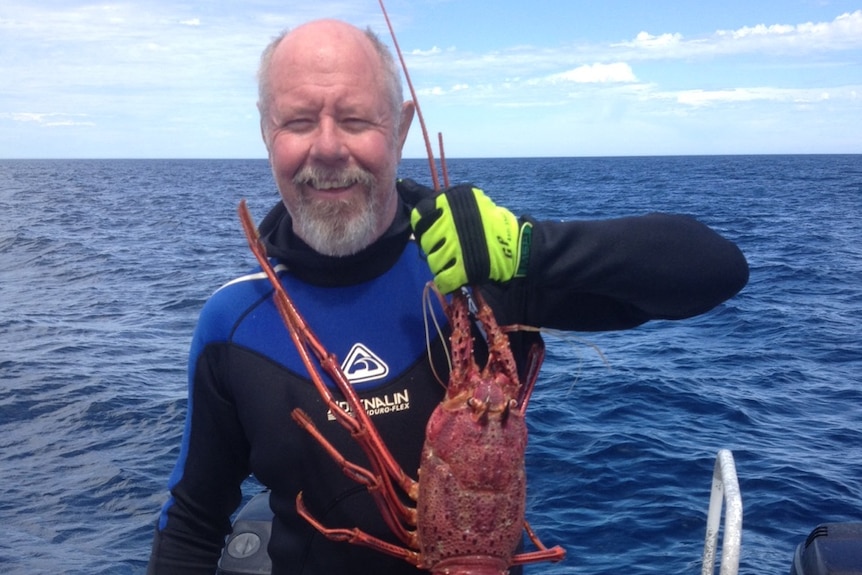 Bret holds up an enormous crayfish in a boat, with seawater in the background.