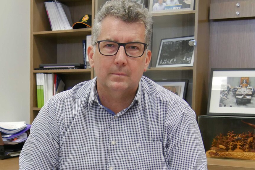 Man with grey, short hair and black glasses sits in an office with a long-sleeved, shirt