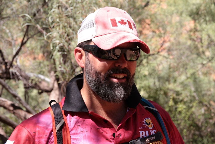 a man with a beard and wearing a pink shirt and cap in the bush