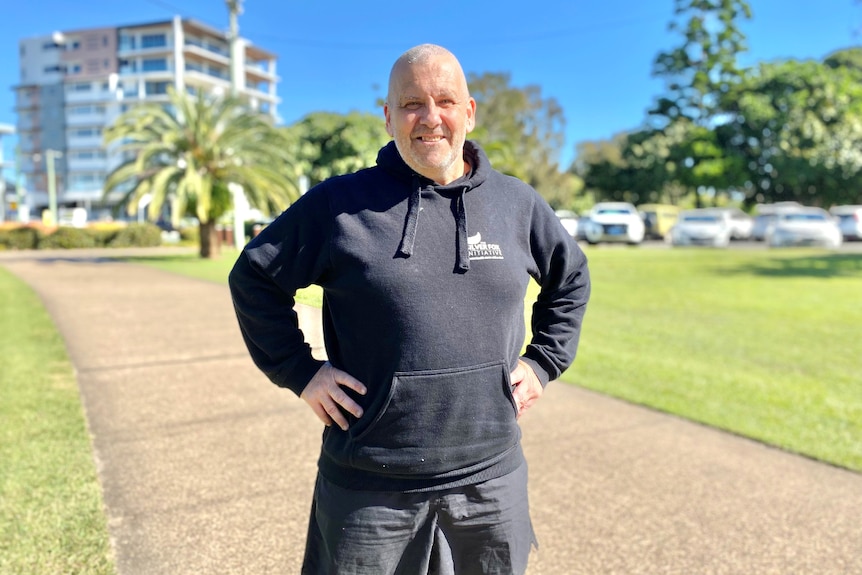 Man stands with hands on hips on walking track, sunny day and smiling