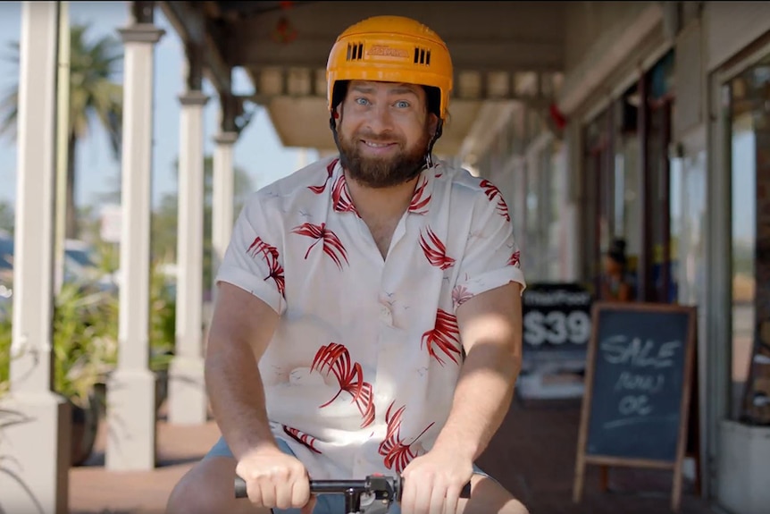 Still from the seafood industry's new television ad showing a man riding a motorised esky in front a row of shops.