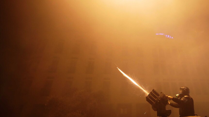 A Riot police officer fires tear gas from a launcher against anti-government protesters trying to enter parliament square during a protest at a road leading to the parliament building in Beirut, Lebanon