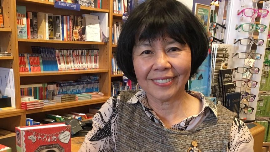 An older east asian woman stands in front of books in a bookshop
