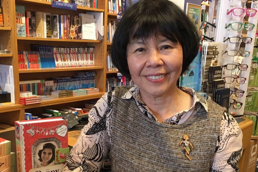 An older east asian woman stands in front of books in a bookshop