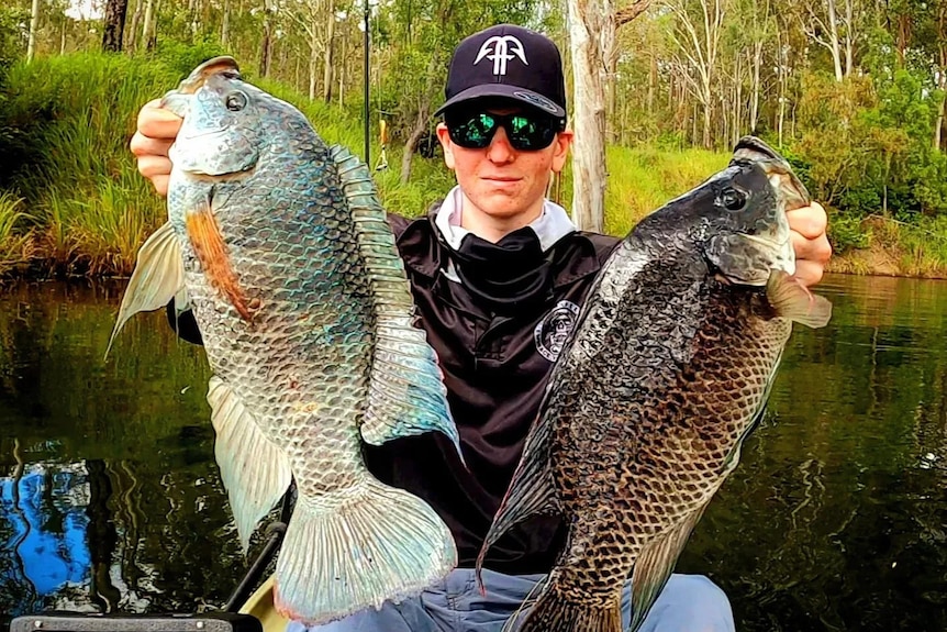 Bloke with sunnies and a cap holds up two large fish.