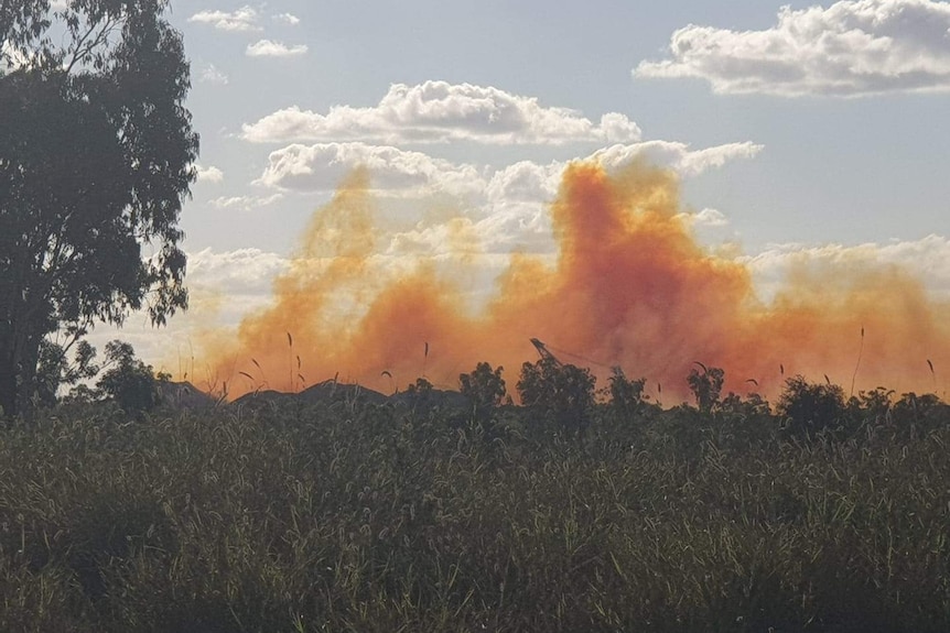 A bright orange plume of smoke rising from piles of coal in the distance.