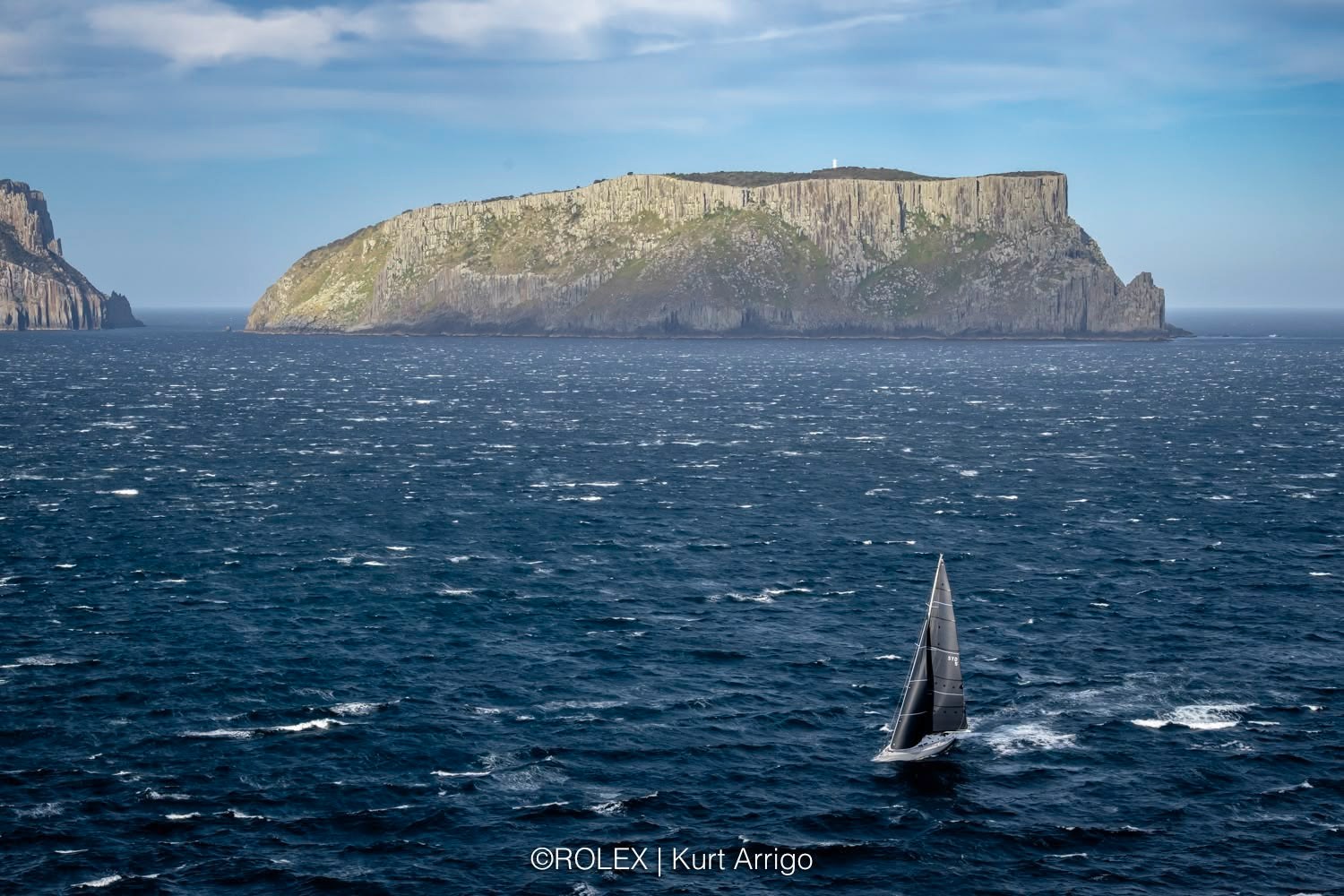 Un yate en el mar con una isla al fondo.