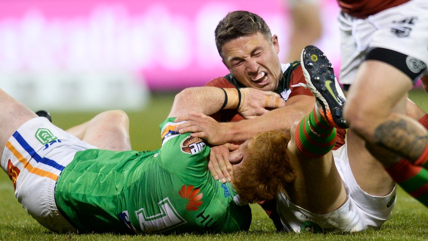 Sam Burgess grimaces and closes his eyes as he lies on the floor and grapples with Corey Horsburgh