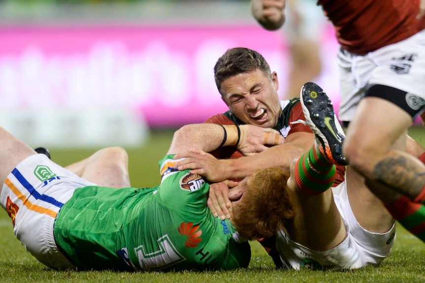 Sam Burgess grimaces and closes his eyes as he lies on the floor and grapples with Corey Horsburgh