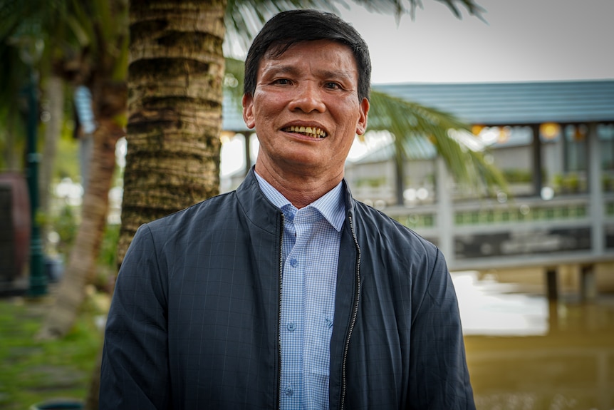 Vietnamese man wearing blue shirt and zipped jacket standing in a sanctuary.