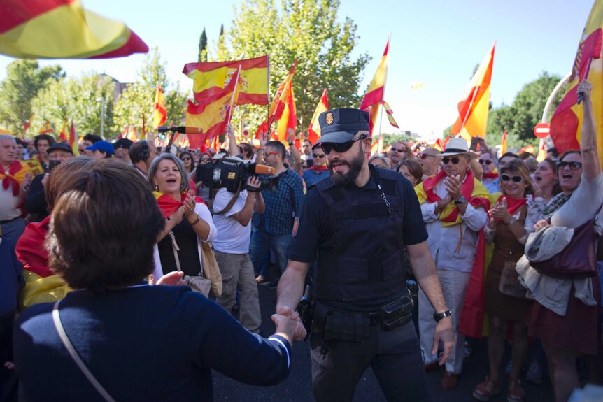 A woman shakes hands with a national police officer in Madrid. Pro-unity protesters are cheering and waving Spanish flags.