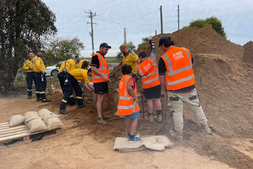 A group of people in SES hi-vis next to a mound of sand, making sandbags