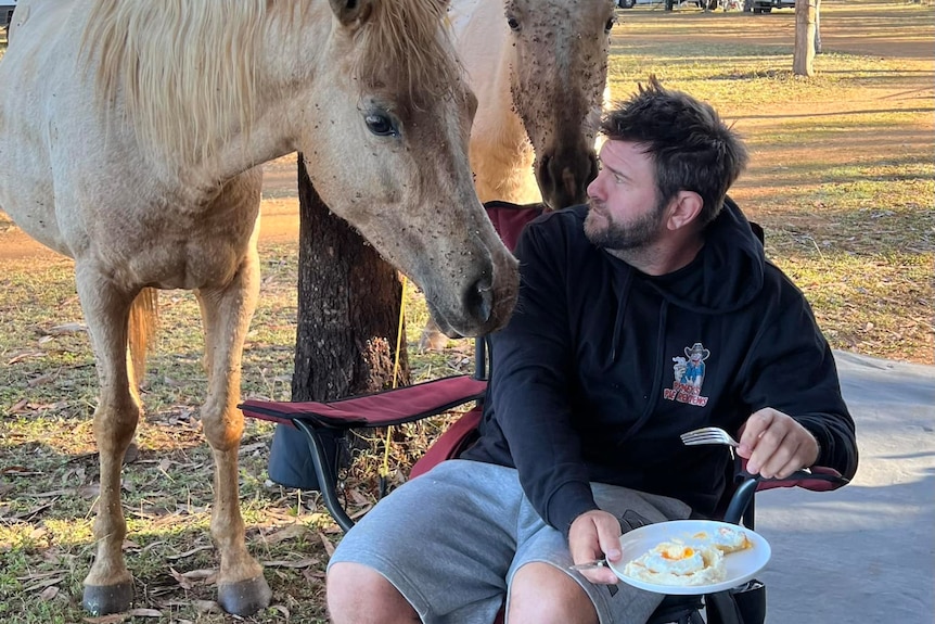 Two horses take interest in Shaun Pyne's breakfast as his pie review tour takes him to Mareeba