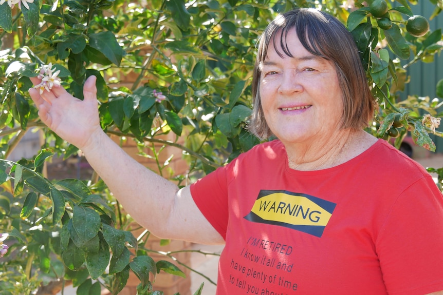 A woman in a red shirt stands in front of a tree 