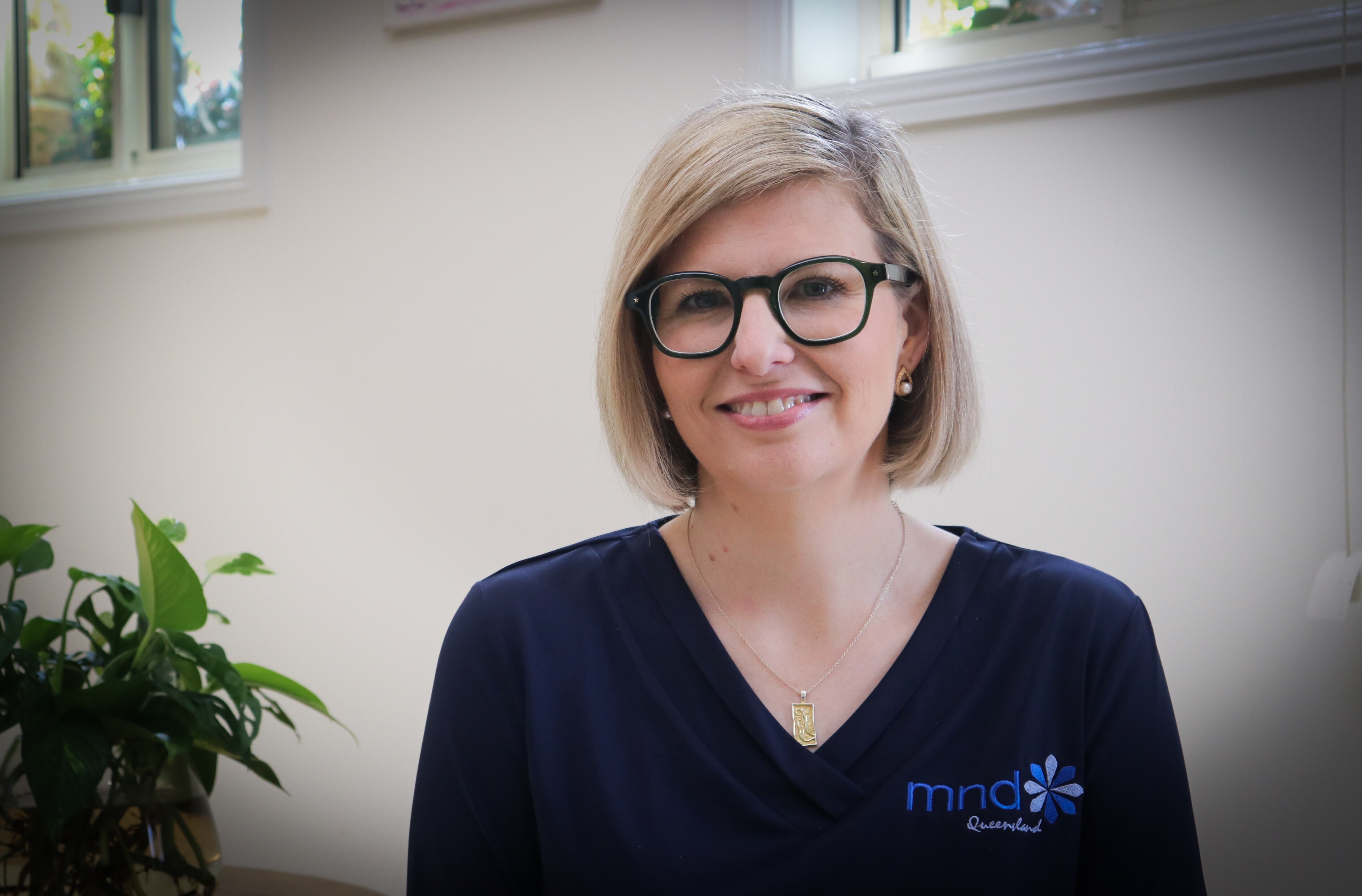 A blonde woman in glasses and dark scrub top smiling at the camera