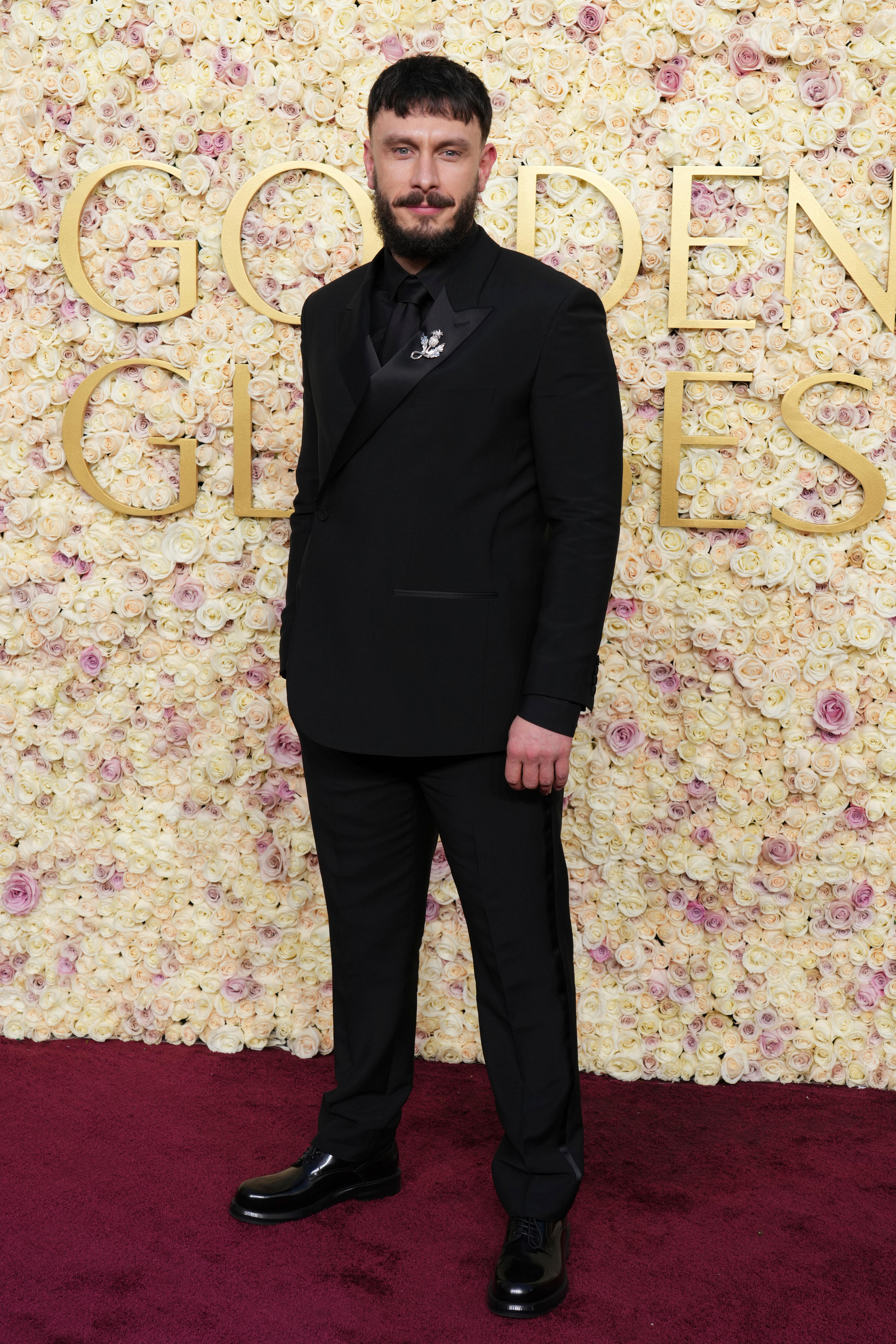 A man in a black suit standing in front of the golden globes sign on the red carpet