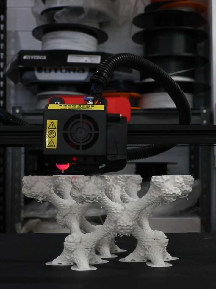 You view a white 3D-print in progress as it stands on a moving black platform.