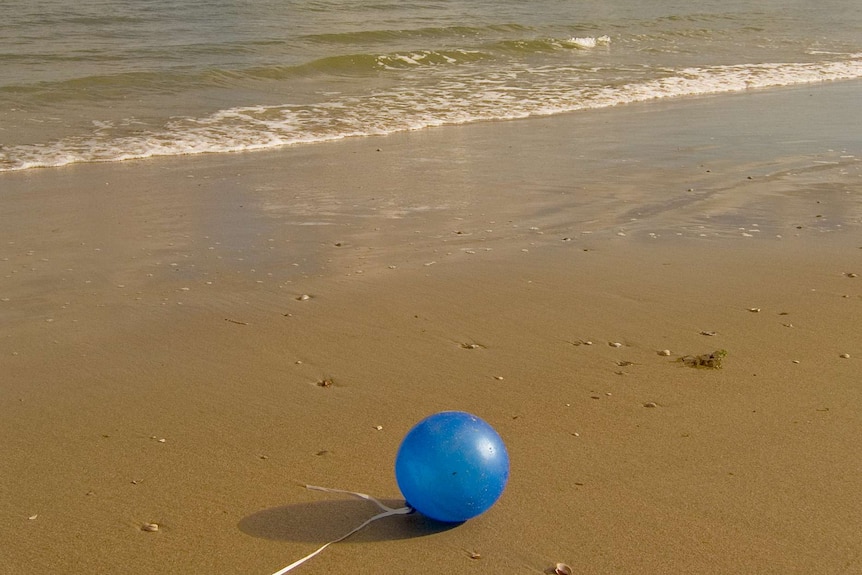 A blue balloon lies on the sand in the surf.
