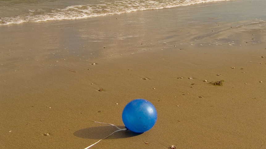 A blue balloon lies on the sand in the surf.