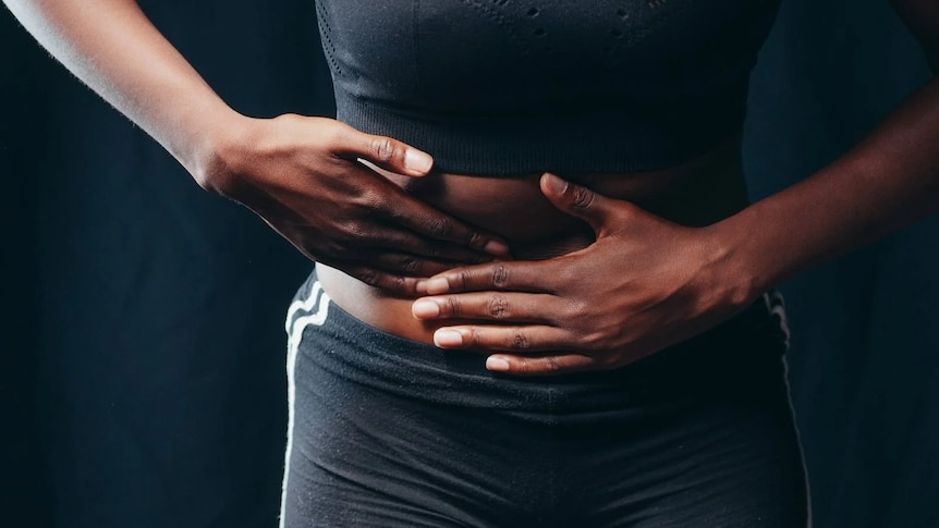 A woman's hands push her stomach. she is wearing black activewear