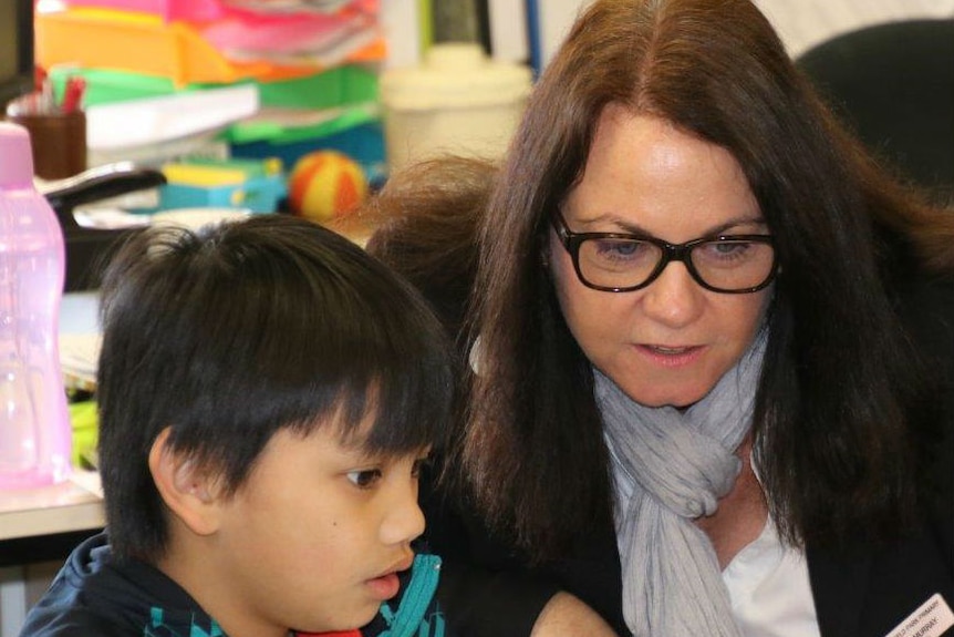 A female teacher wearing glasses helps a young boy on his lap top