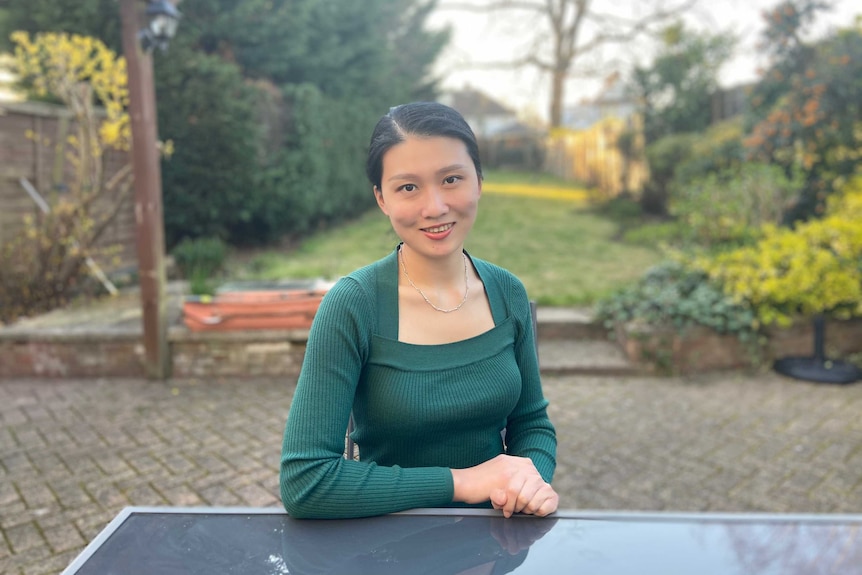 英国华人Esther Hu坐在一个后院里，身前有一张桌子。