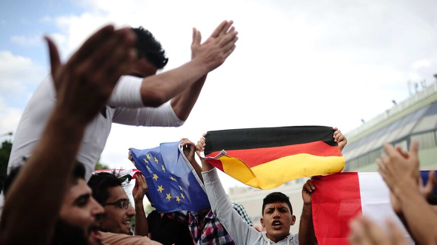 Syrian migrants shout slogans as they hold flags of Germany