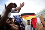 Syrian migrants shout slogans as they hold flags of Germany