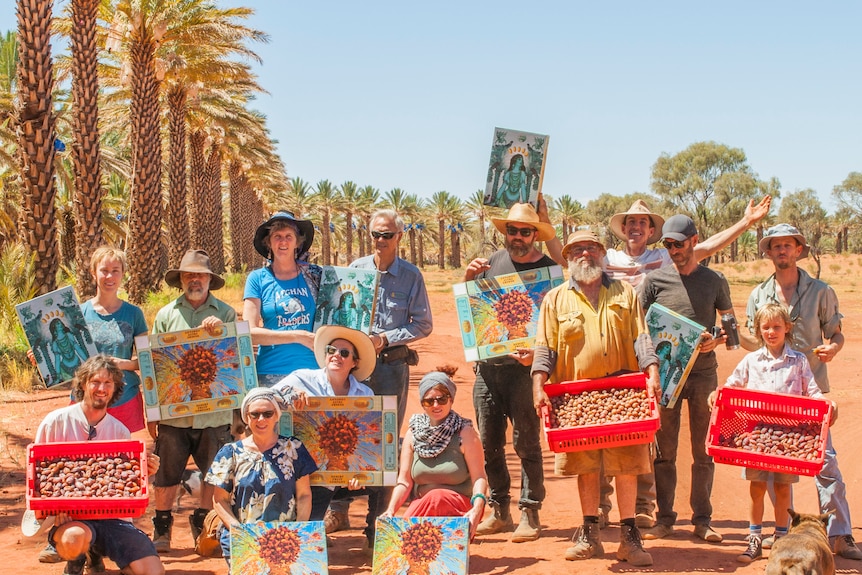 13 adults and one child stand holding boxes of dates harvested on a Northern Territory farm