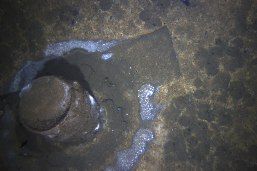 A barrel on muddy seafloor with white contents spilling.