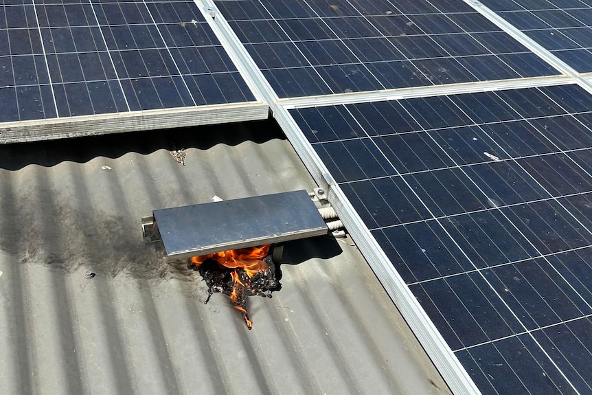 Small flames coming from a box next to solar panels on a roof