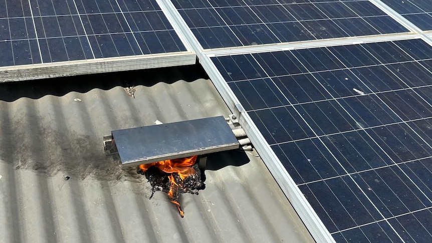 Small flames coming from a box next to solar panels on a roof