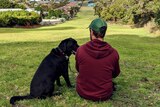 a man sits on a hill with his guide dog