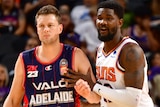 An Adelaide 36ers players leans against a Phoenix Suns player in a preseason game.