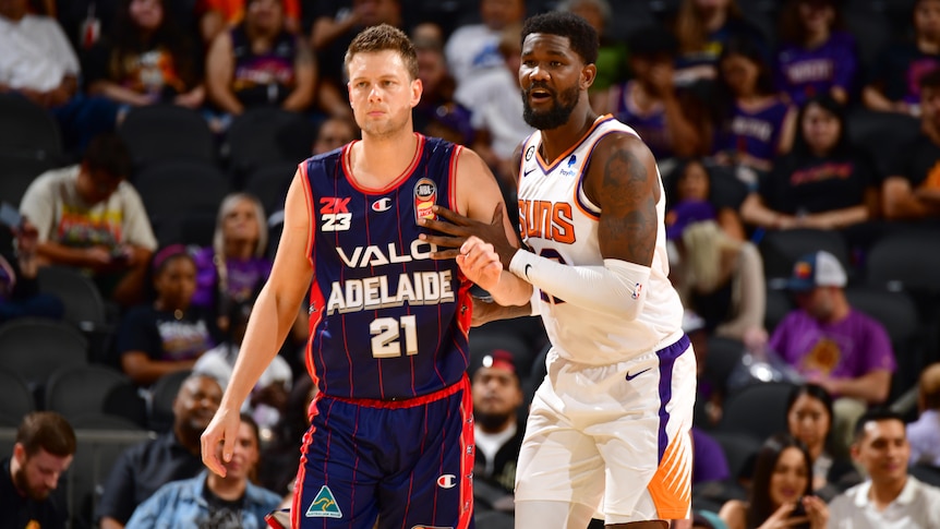 An Adelaide 36ers players leans against a Phoenix Suns player in a preseason game.