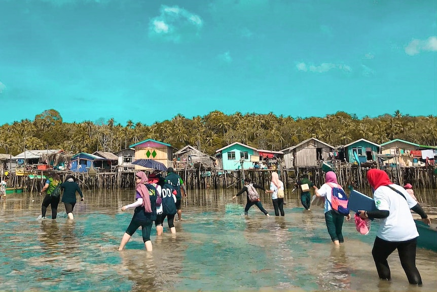 Huts sitting in on silts in the water as people wander past.