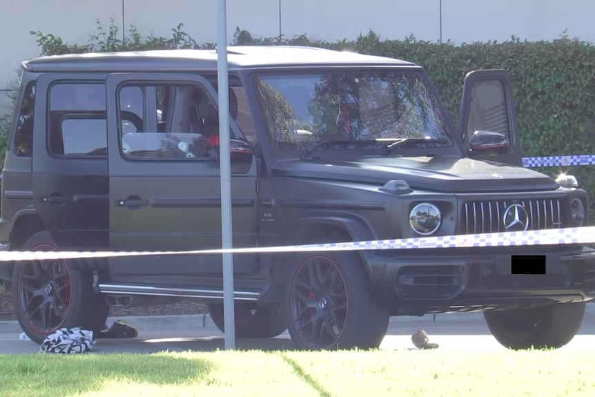 A black Mercades 4wd-style car behind police tape, with bullet holes visible in the driver-side window.