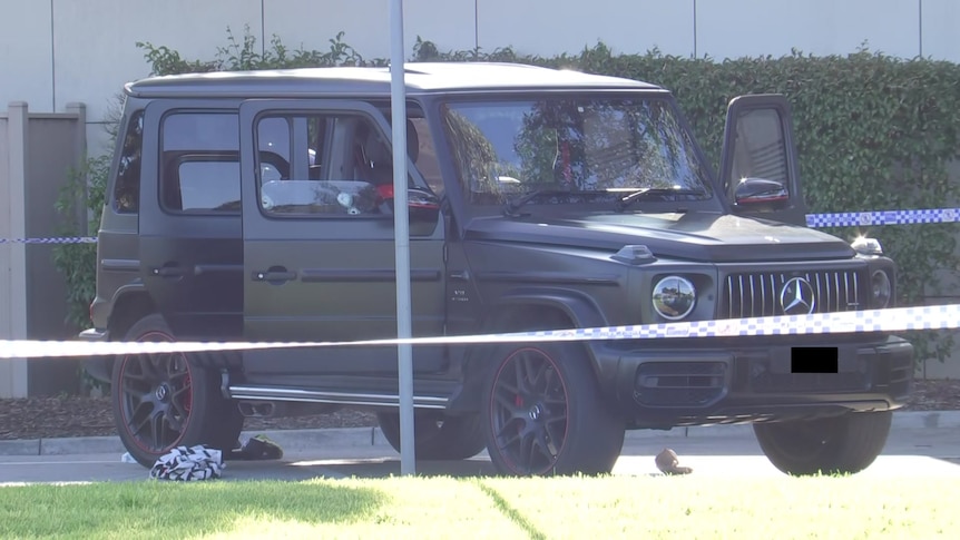 A black Mercades 4wd-style car behind police tape, with bullet holes visible in the driver-side window.