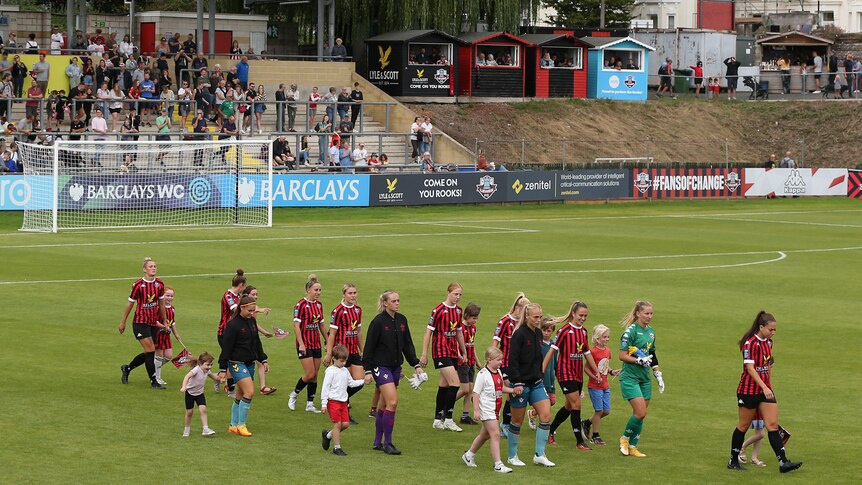 A women's soccer team wearing red and black walks out onto a field