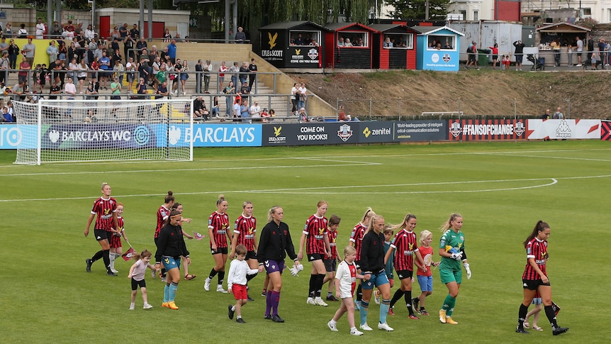 A women's soccer team wearing red and black walks out onto a field