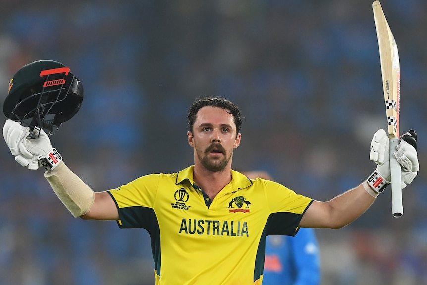 Travis Head raises his bat and helmet after making a century for Australia.