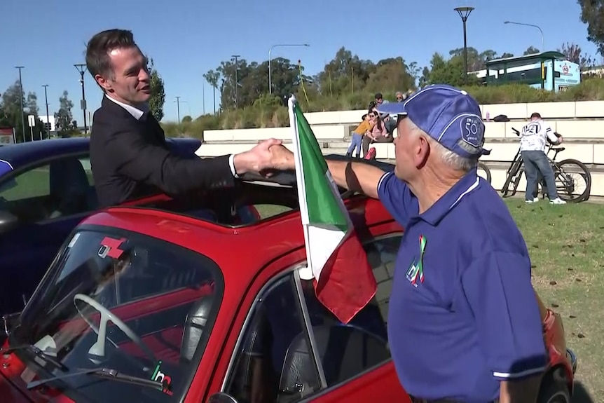 a man shaking another man's hand over a car