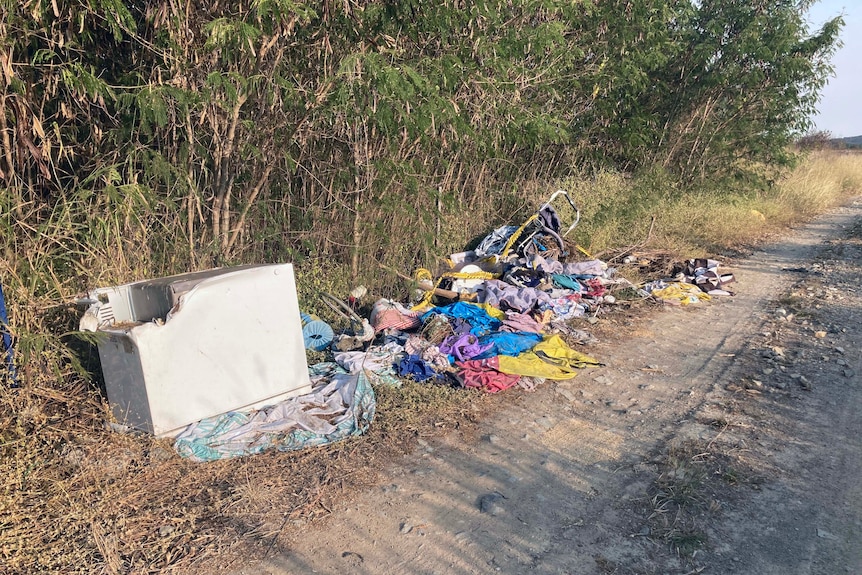 Waste dumped on the side of a dirt road next to bushland