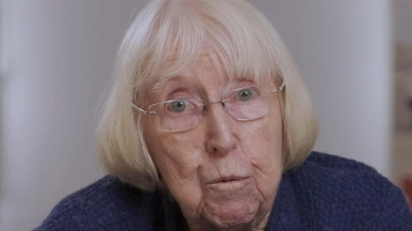 A close-up of Merle Mitchell, an elderly woman with white hair, blue eyes and a blue top.