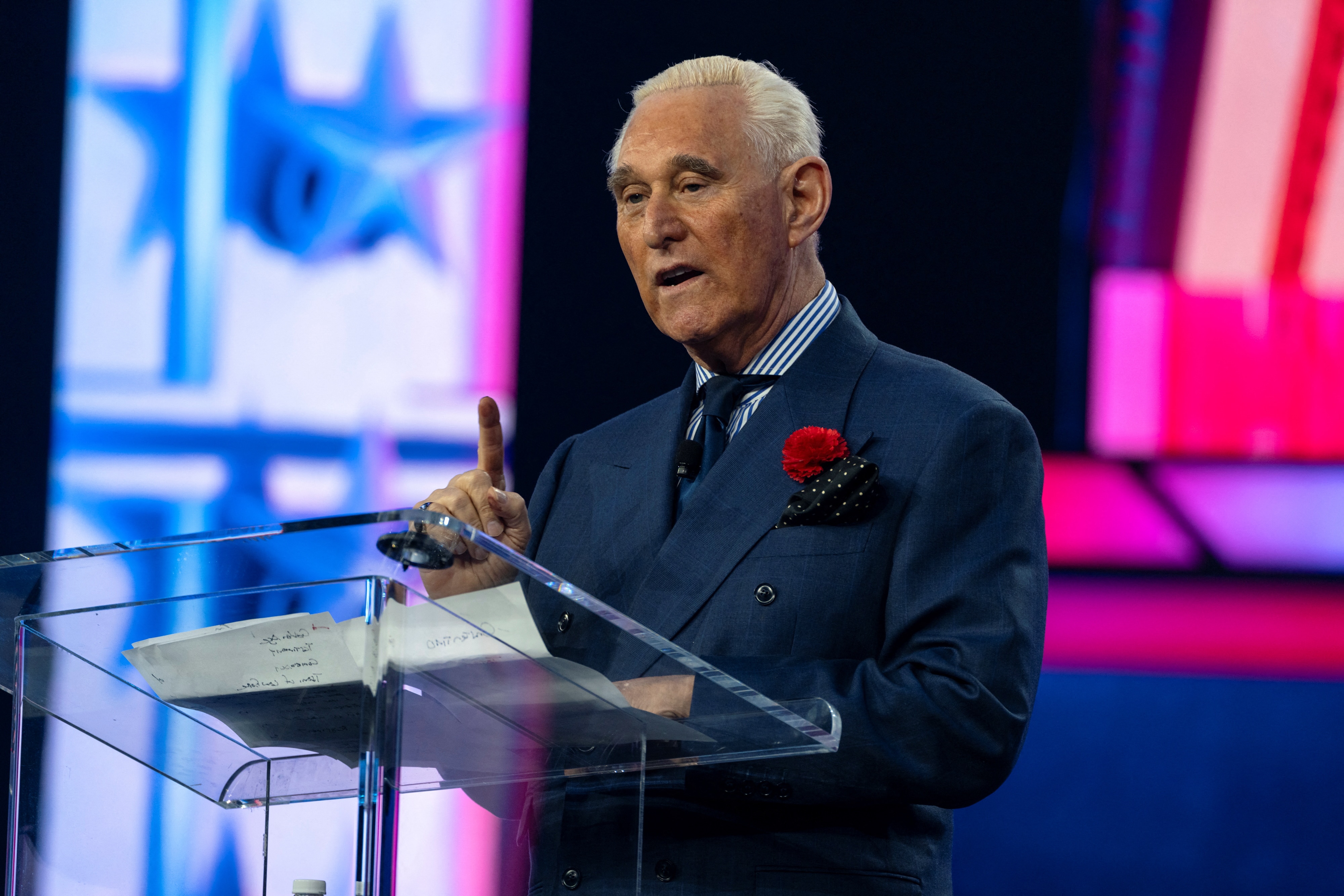 Roger Stone stands at a transparent podium and speaks.