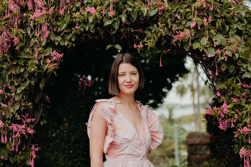 A young woman with a bob haircut wearing a pink dress standing in a garden surrounded by pink flowers