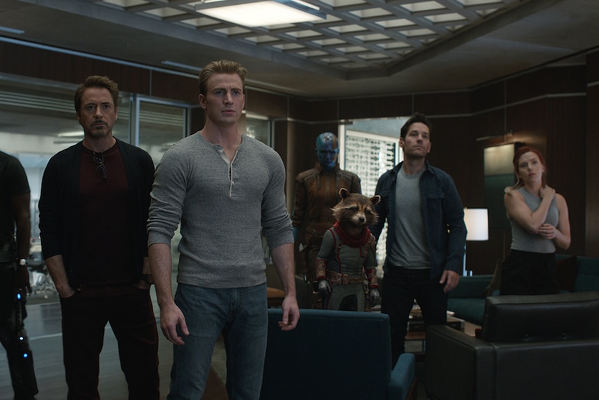 Colour still of the cast of Avengers: Endgame standing as a group in a room.