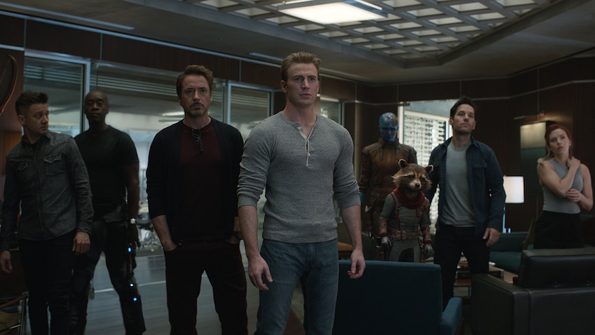 Colour still of the cast of Avengers: Endgame standing as a group in a room.